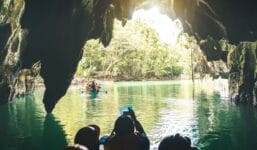Adventurers on a boat tour inside the Puerto Princesa Underground River in Palawan, Philippines, are surrounded by limestone caves and clear green water. This location is a top UNESCO World Heritage Site and a popular destination.